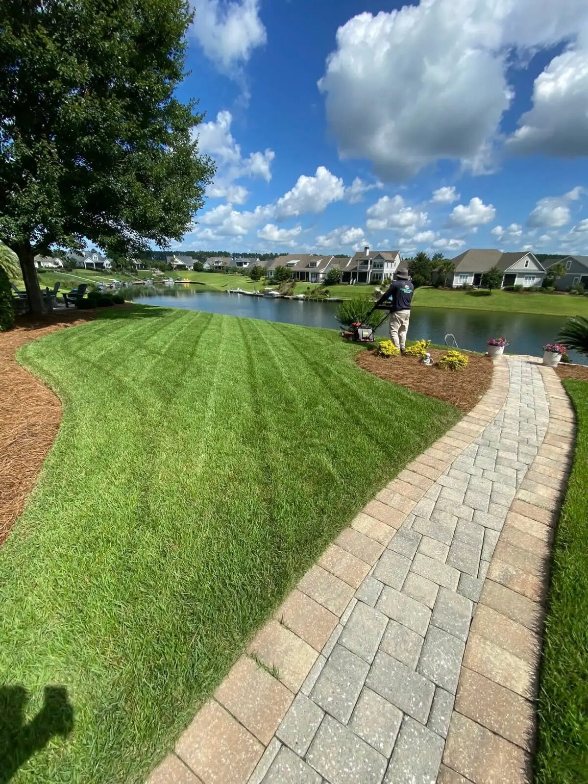 Striped lakeside lawn being mowed beside a paver path and flower planters